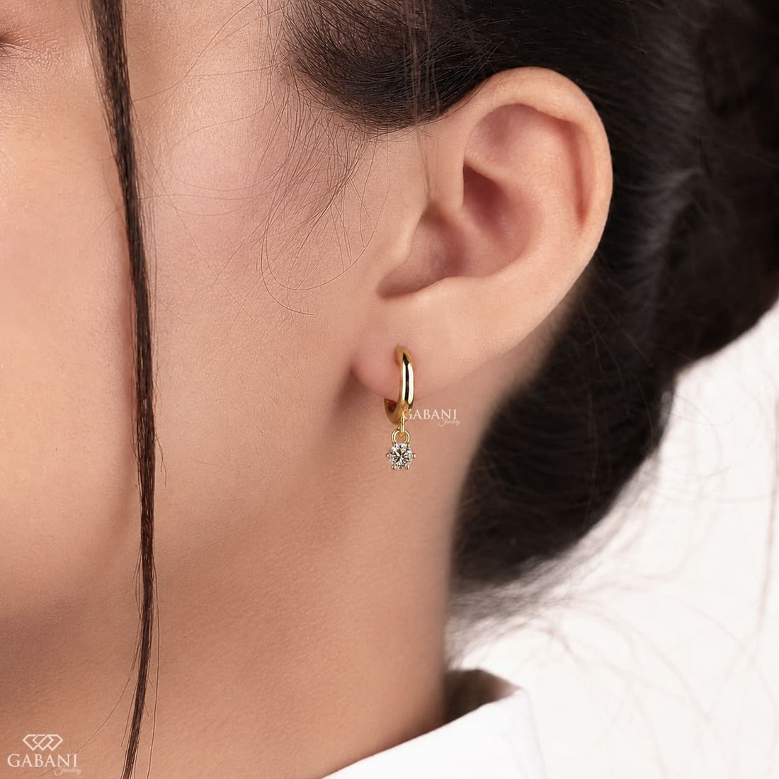 Round lab grown diamond charm huggie hoop earrings with approx. 2.3 mm prong-set dangling diamonds and hinged closure in polished gold.