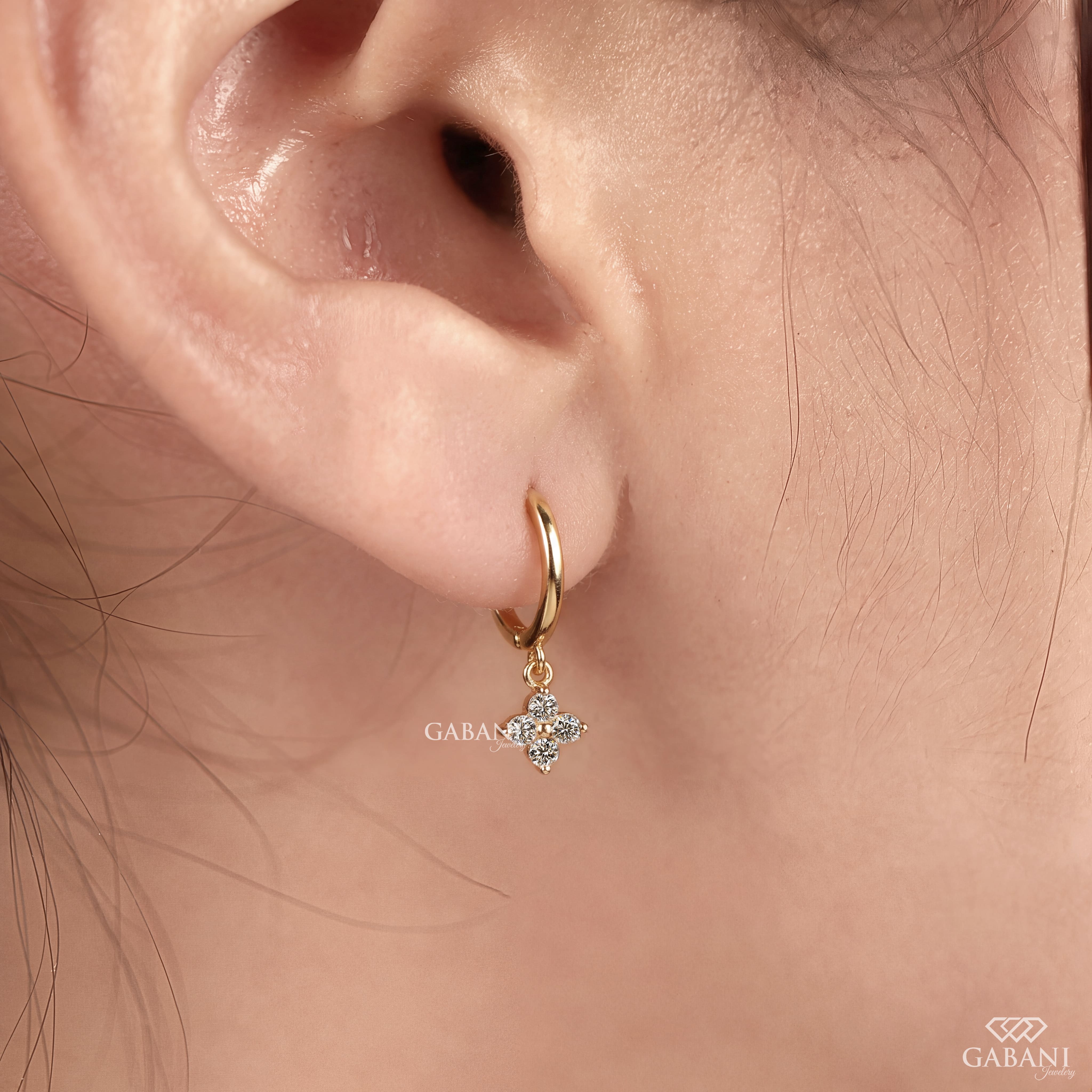 Close-up of round cut lab grown diamond flower charm huggie hoop earrings with four stone floral clusters in polished 18K yellow gold.