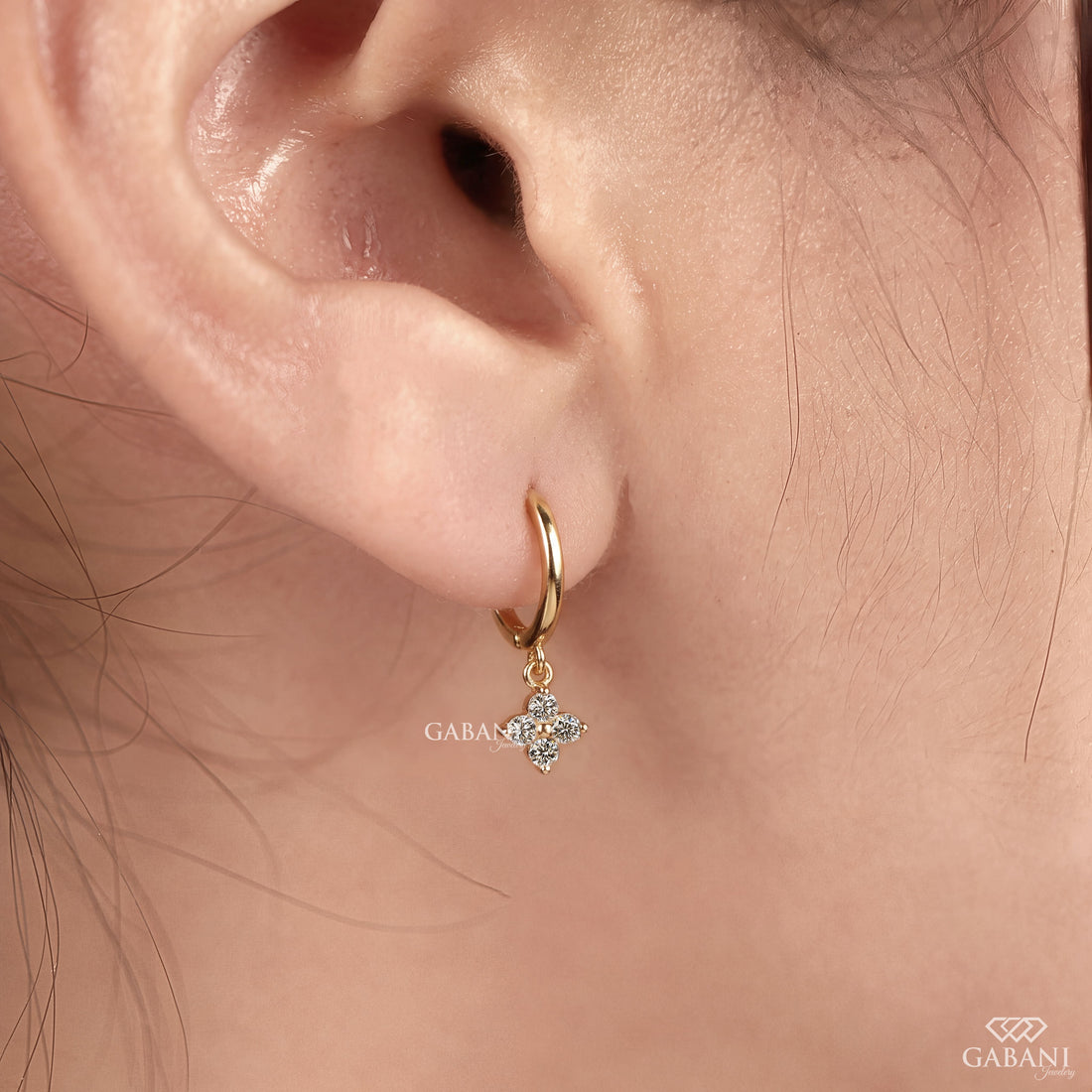 Close-up of round cut lab grown diamond flower charm huggie hoop earrings with four stone floral clusters in polished 18K yellow gold.