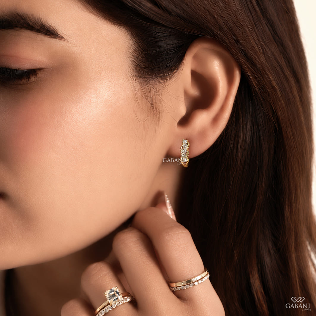 Round diamond infinity huggie hoop earrings in yellow gold with five diamonds and curved gold loop detailing.