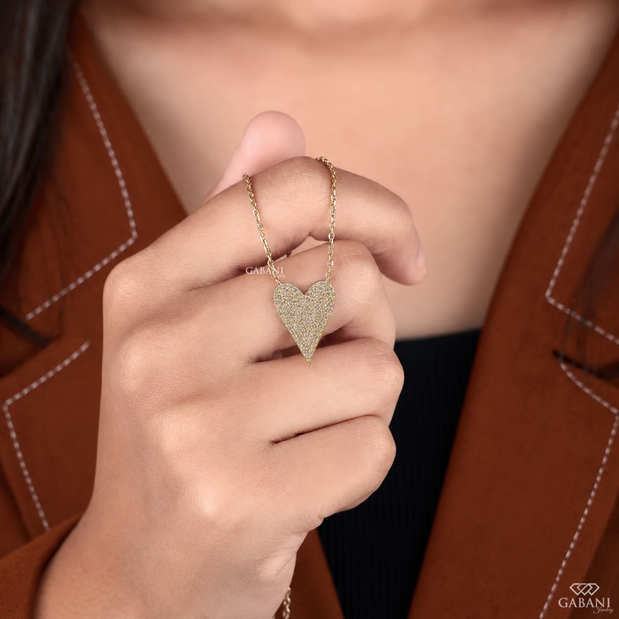 Close-up of an asymmetrical heart shaped lab grown diamond necklace featuring round cut pavé diamonds set in yellow gold.