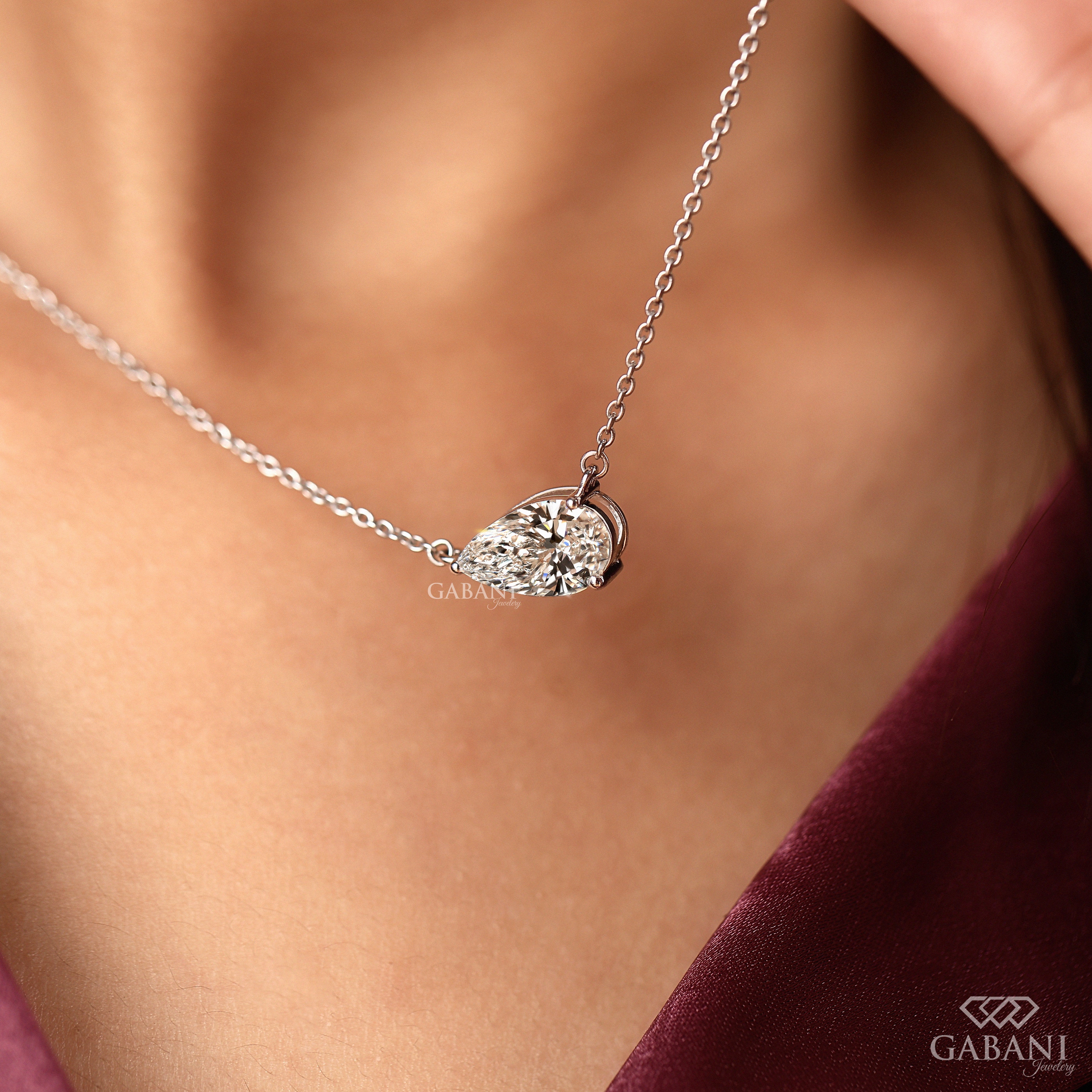 Silver necklace with a teardrop-shaped pendant on a blurred background, featuring the GABANI brand.