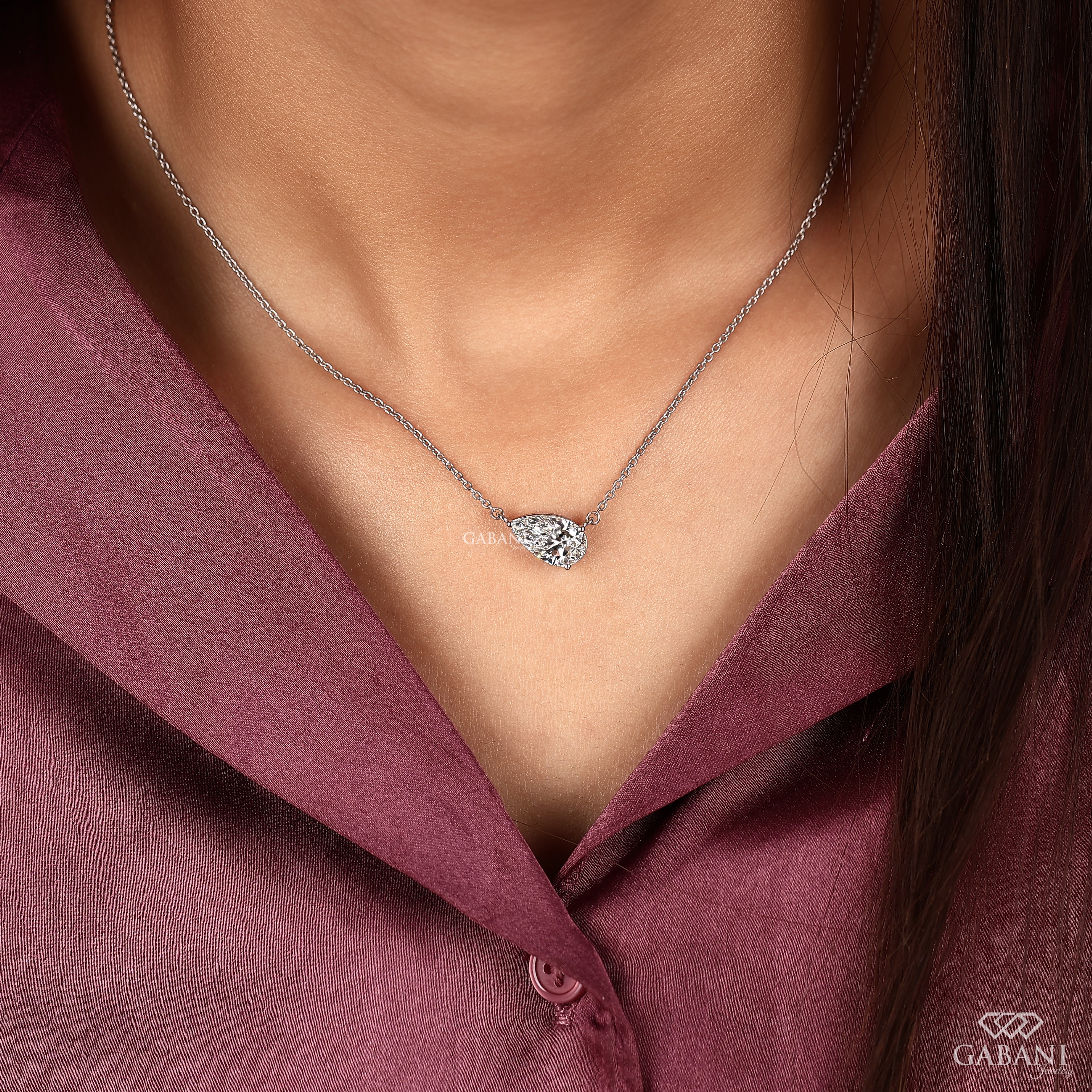 Necklace with a heart-shaped diamond pendant worn by a person in a pink shirt, with 'GABANIL' branding.
