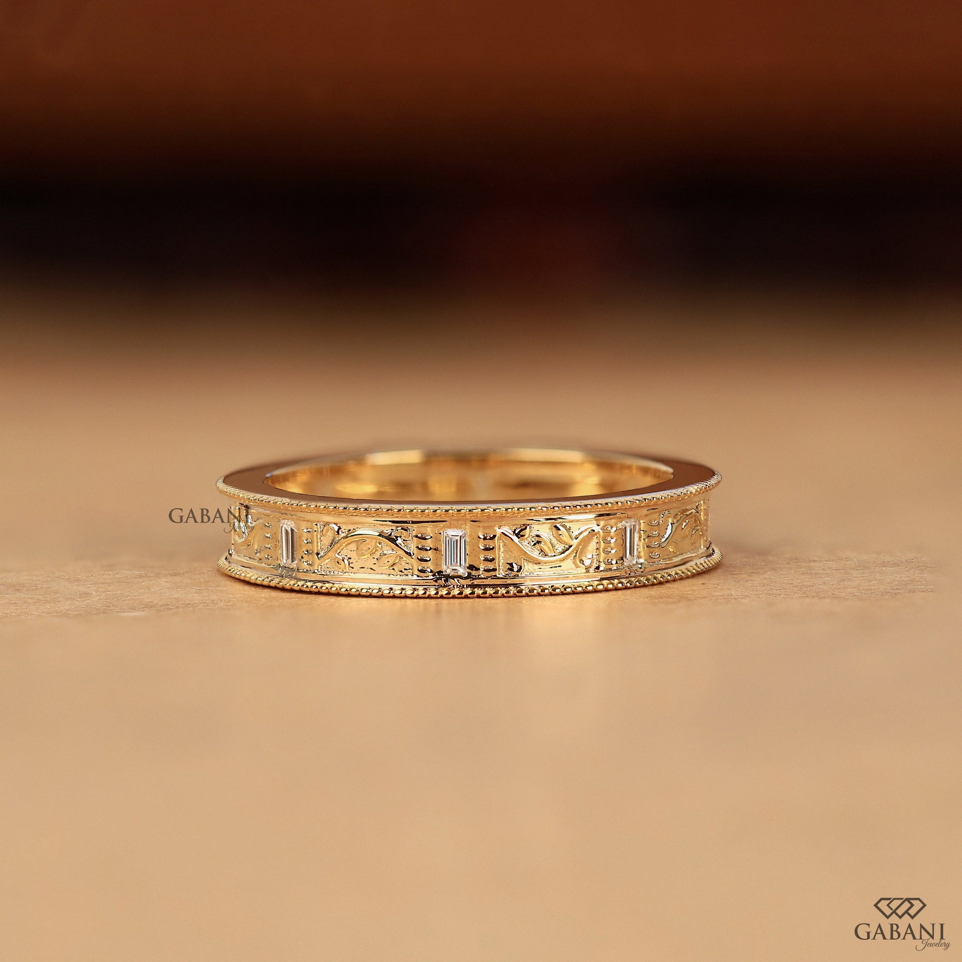 GABANIJEWELRY milgrain art deco wedding band on hand in yellow gold, leaf inspired design with engraved details and subtle diamond accents