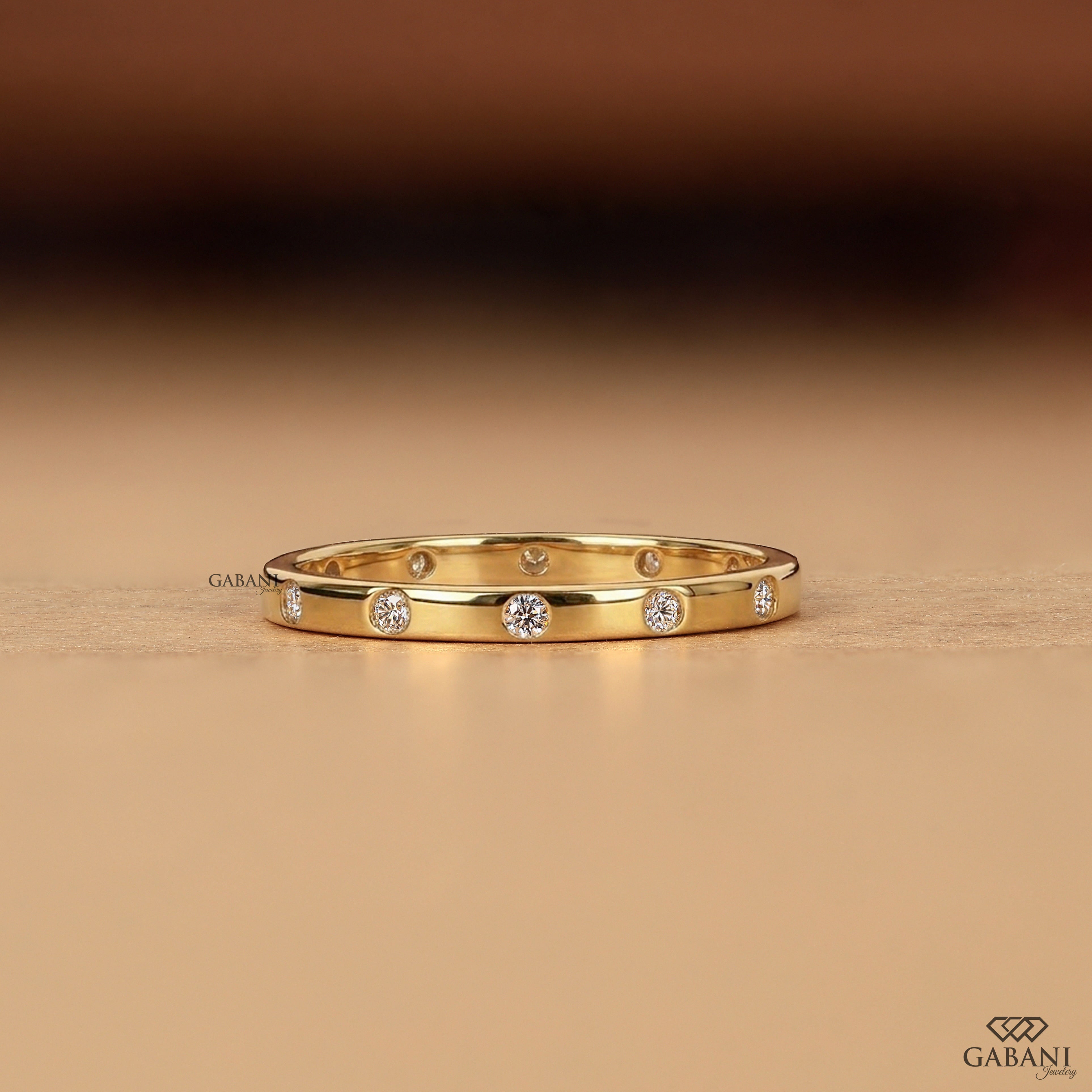 a minimalist lab grown diamond wedding band featuring round cut diamonds individually flush set into polished 14K yellow gold, creating a modern eternity ring perfect for bridal stacking.