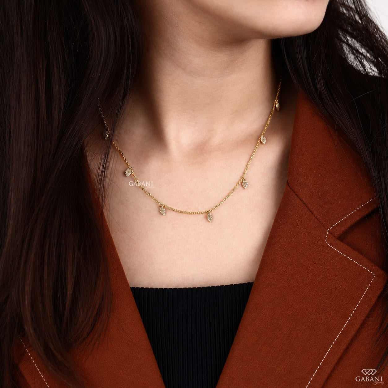 Yellow gold station necklace with multiple dangling pavé diamond leaf charms and a delicate chain, displayed on a wooden surface.