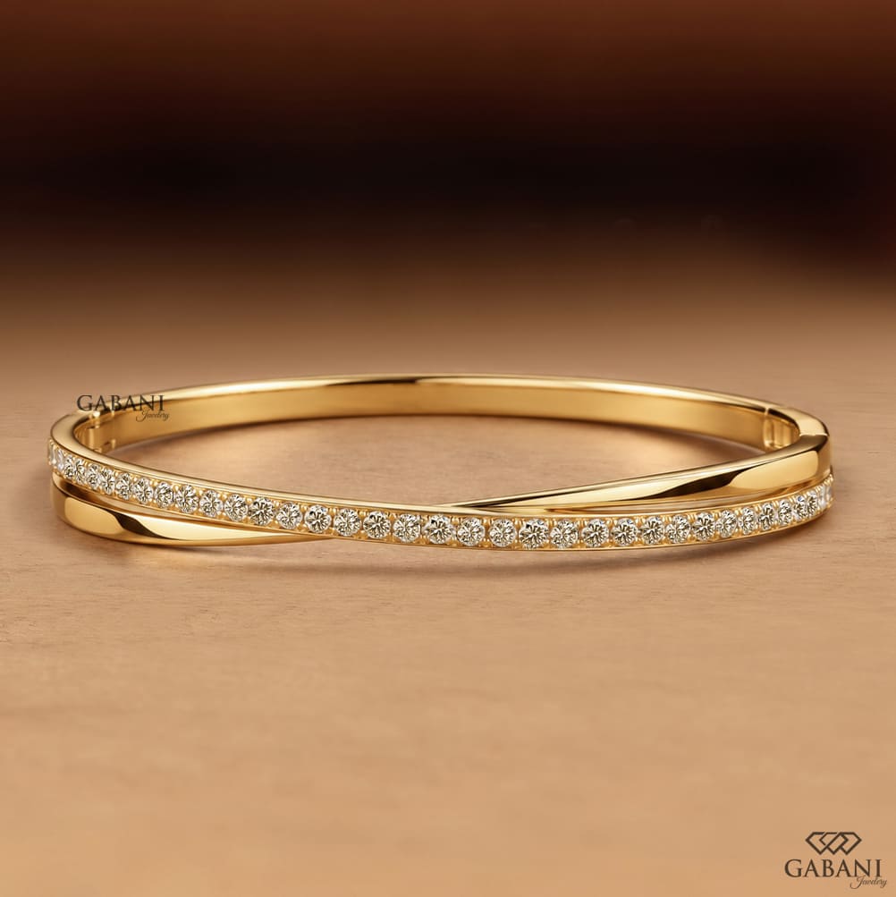 Yellow gold crossover twist bangle bracelet featuring a polished gold band intertwined with a curved row of sparkling round pavé set diamonds.