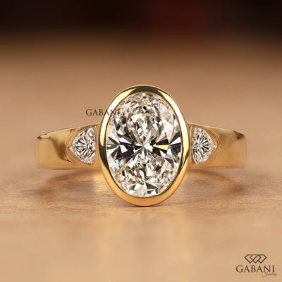Front view of an oval cut lab grown diamond three stone engagement ring with a bezel set center and trillion side diamonds in solid yellow gold
