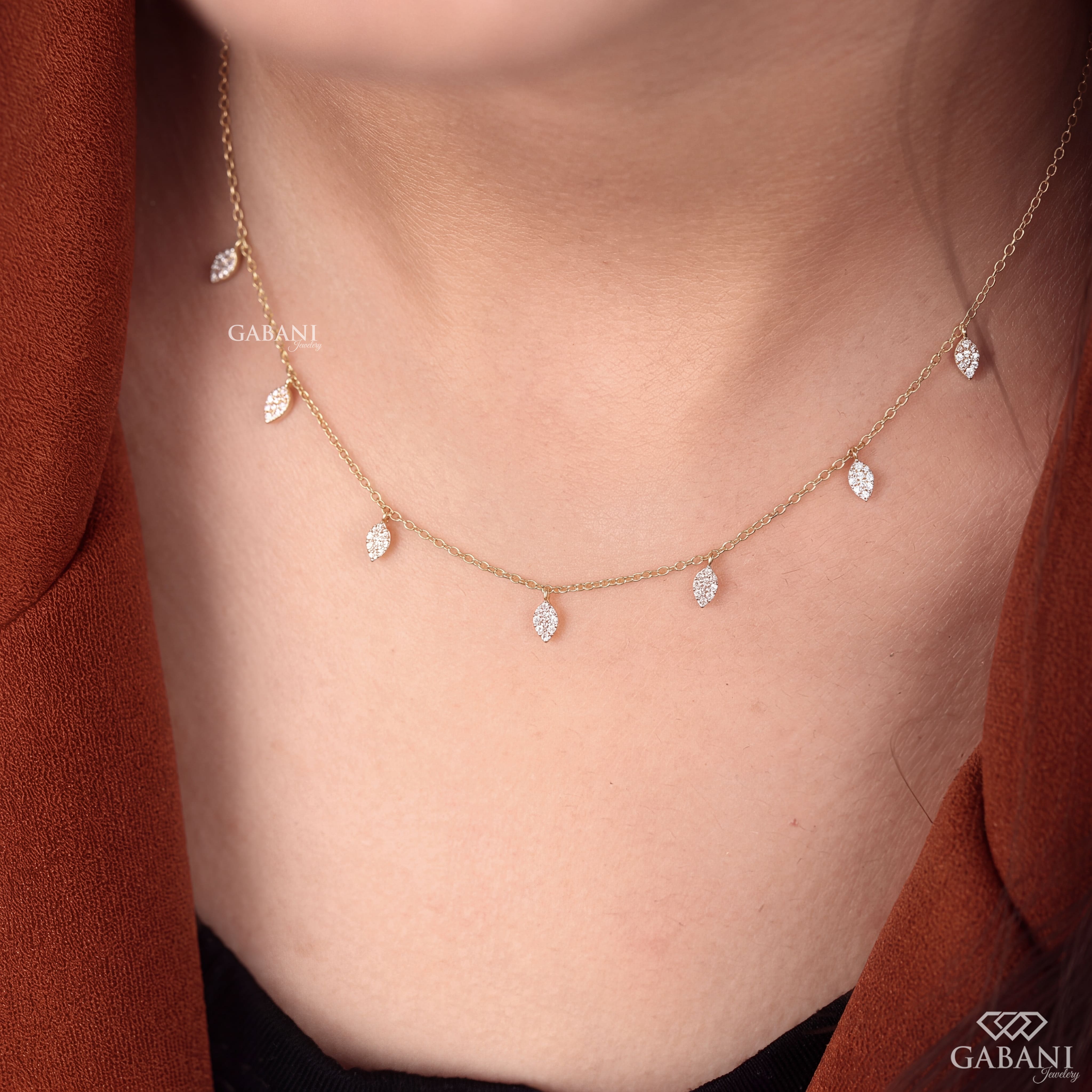 Yellow gold station necklace with multiple dangling pavé diamond leaf charms and a delicate chain, displayed on a wooden surface.
