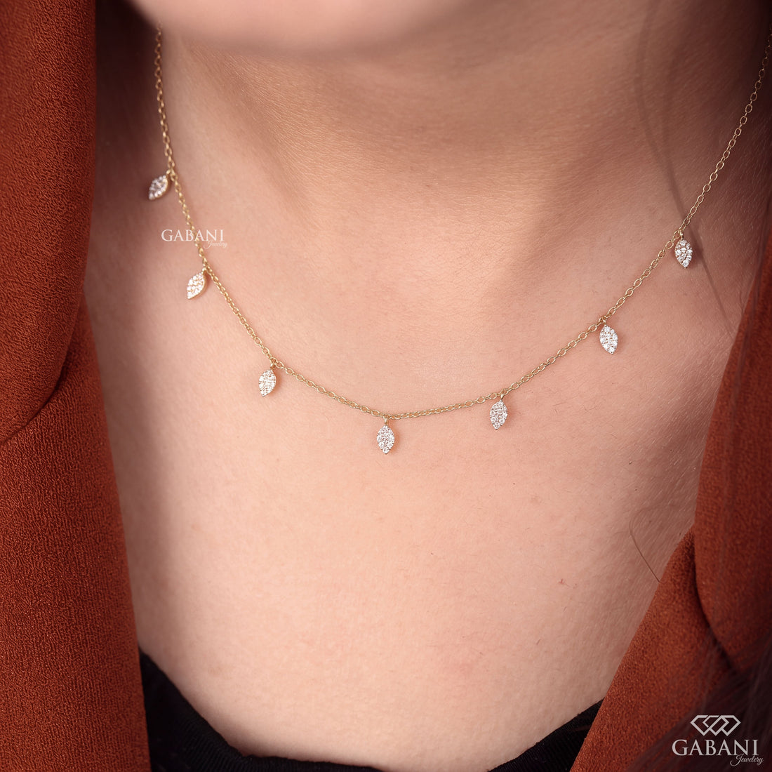 Yellow gold station necklace with multiple dangling pavé diamond leaf charms and a delicate chain, displayed on a wooden surface.