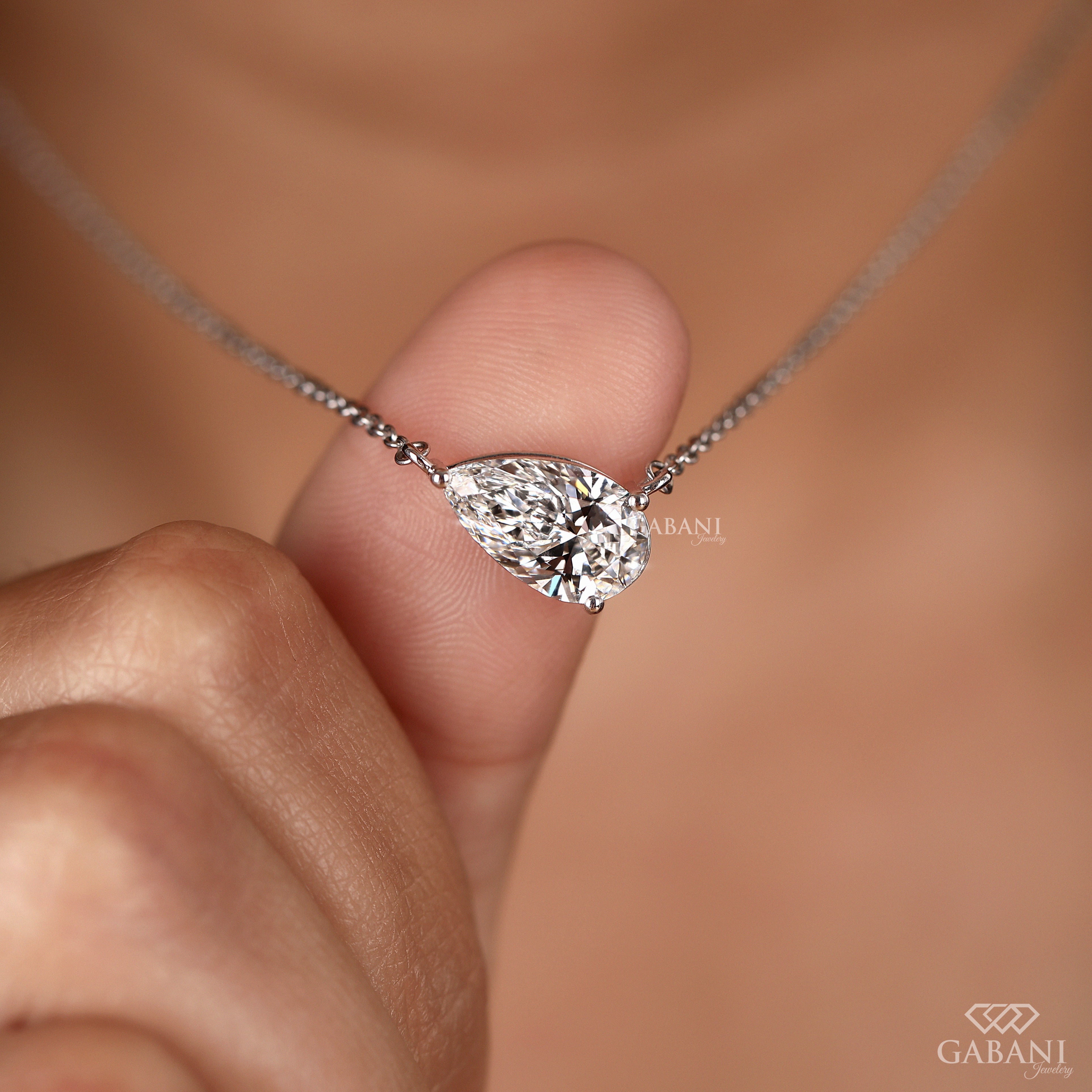 Teardrop-shaped diamond necklace held by a hand with 'GABANI' branding.