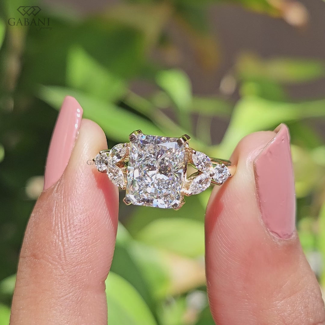 Radiant cut lab grown diamond engagement ring with marquise and round side diamond accents in a nature inspired gold setting.