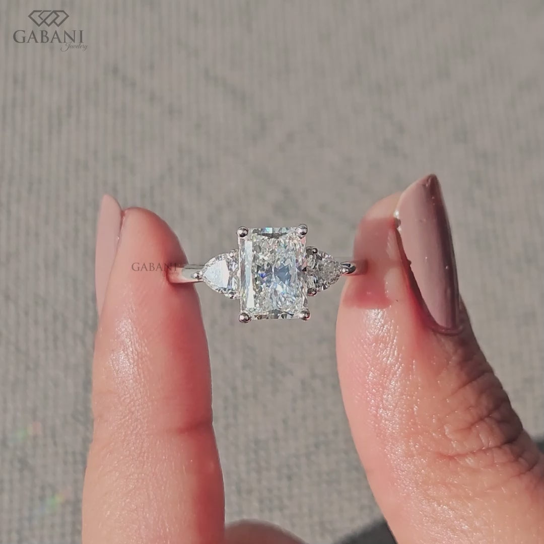 Radiant cut lab grown diamond three stone engagement ring with pear side diamonds, classic prong setting and polished gold band.