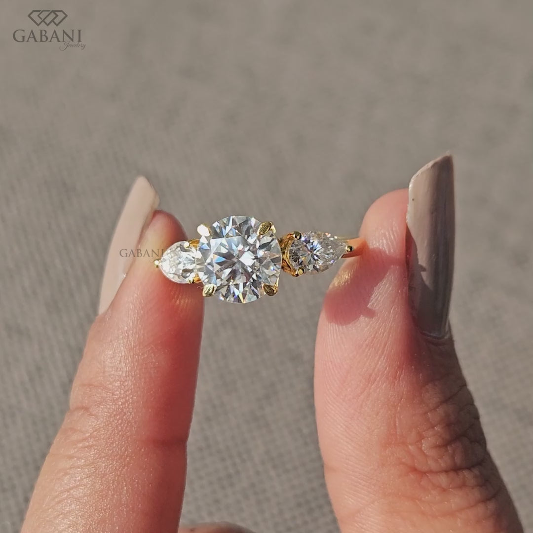 round cut three stone lab grown diamond ring with pear side stones in 14k yellow gold cathedral shank