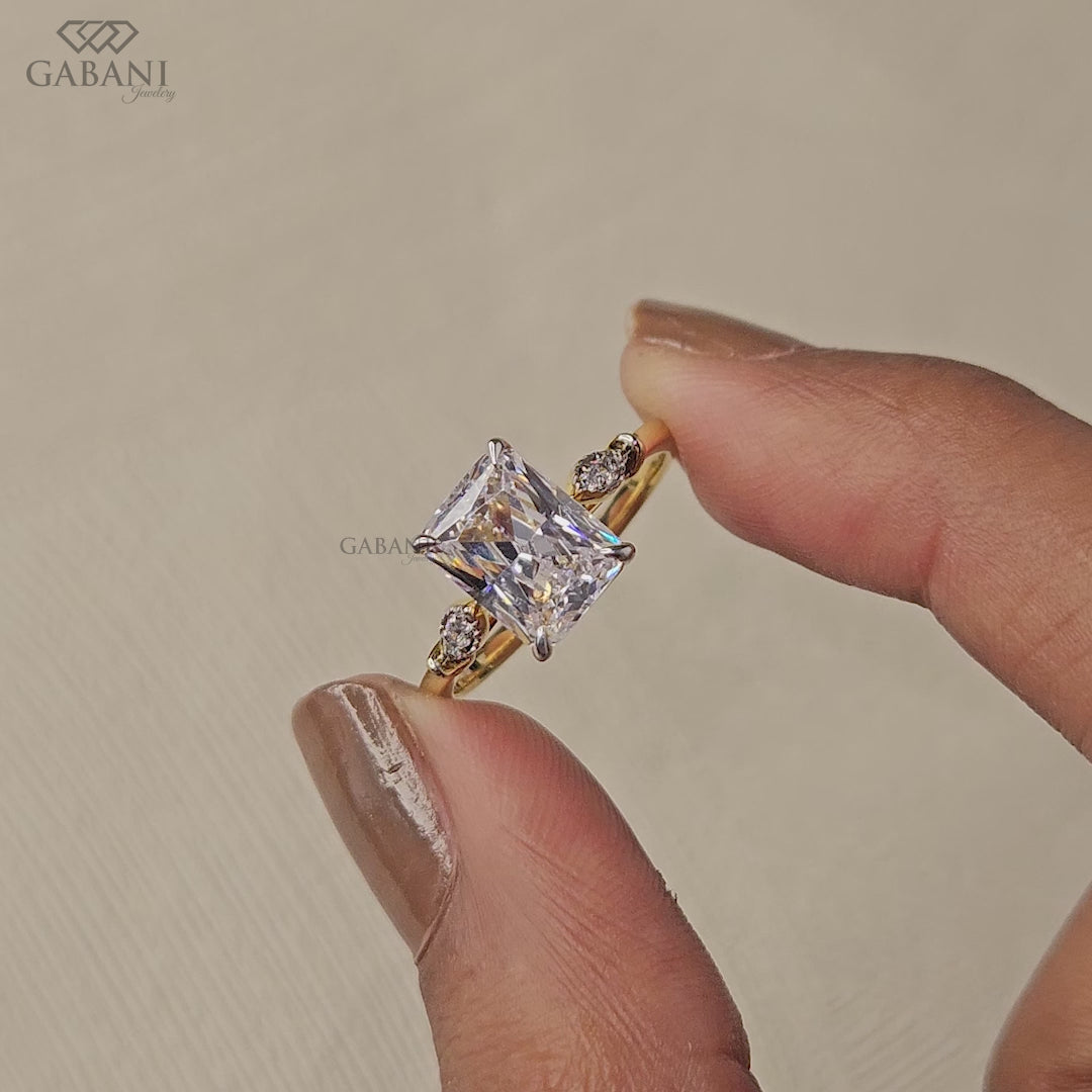 Radiant cut lab grown diamond engagement ring with round side diamond clusters, four prong setting and polished gold band.