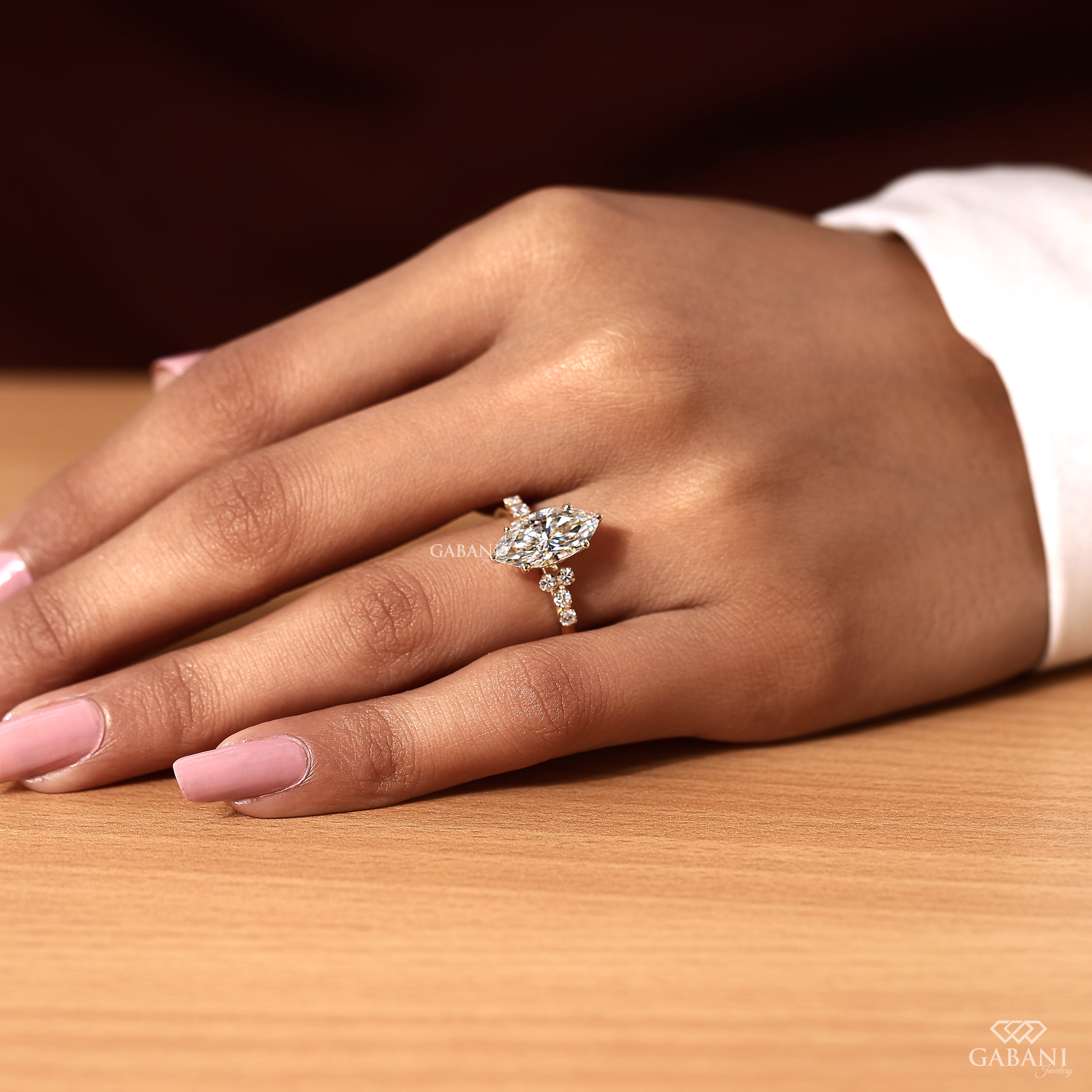 A close-up of a hand wearing a gold-toned marquise-cut diamond ring with small side diamonds, resting on a wooden surface.