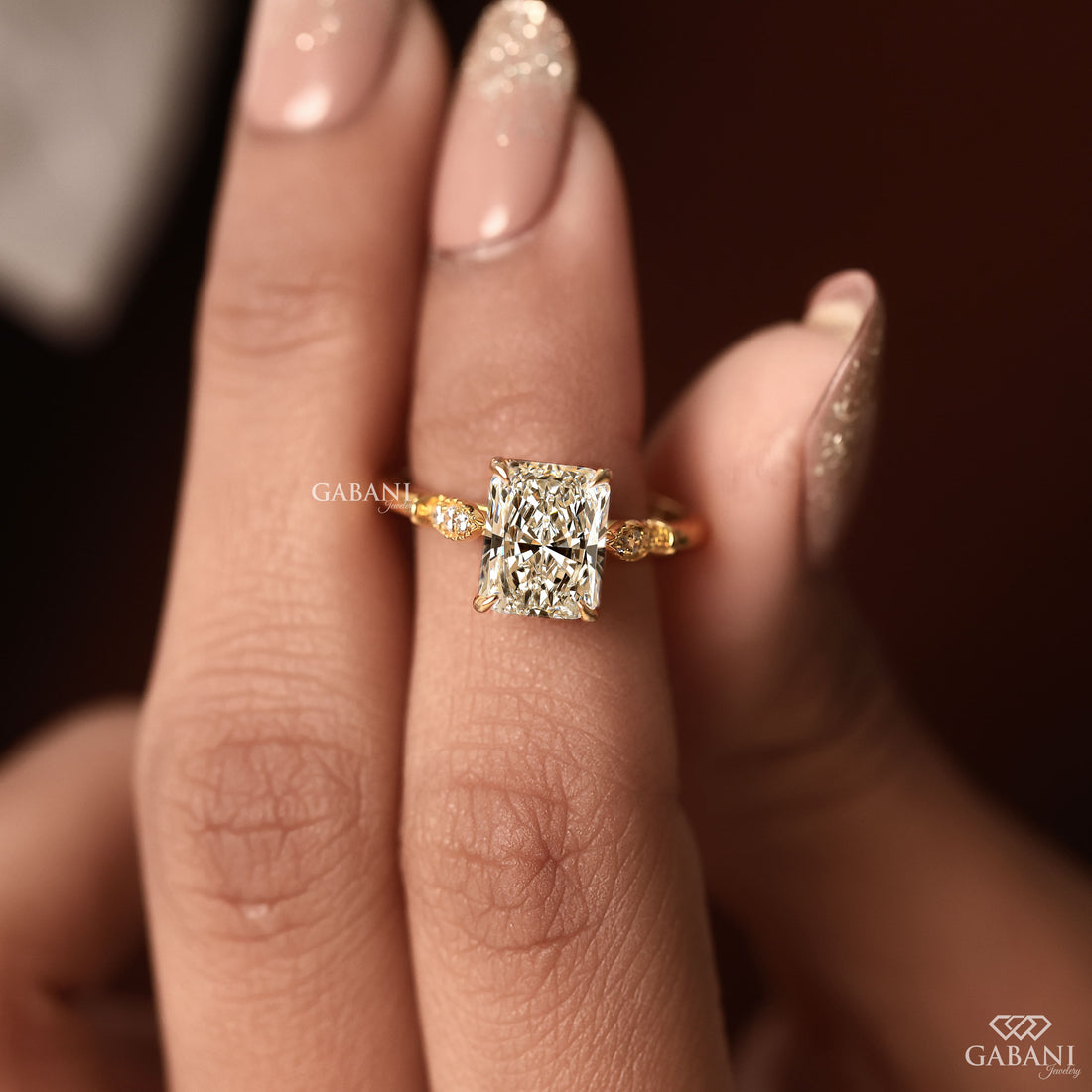 Radiant cut lab grown diamond engagement ring with round side diamond clusters, four prong setting and polished gold band.
