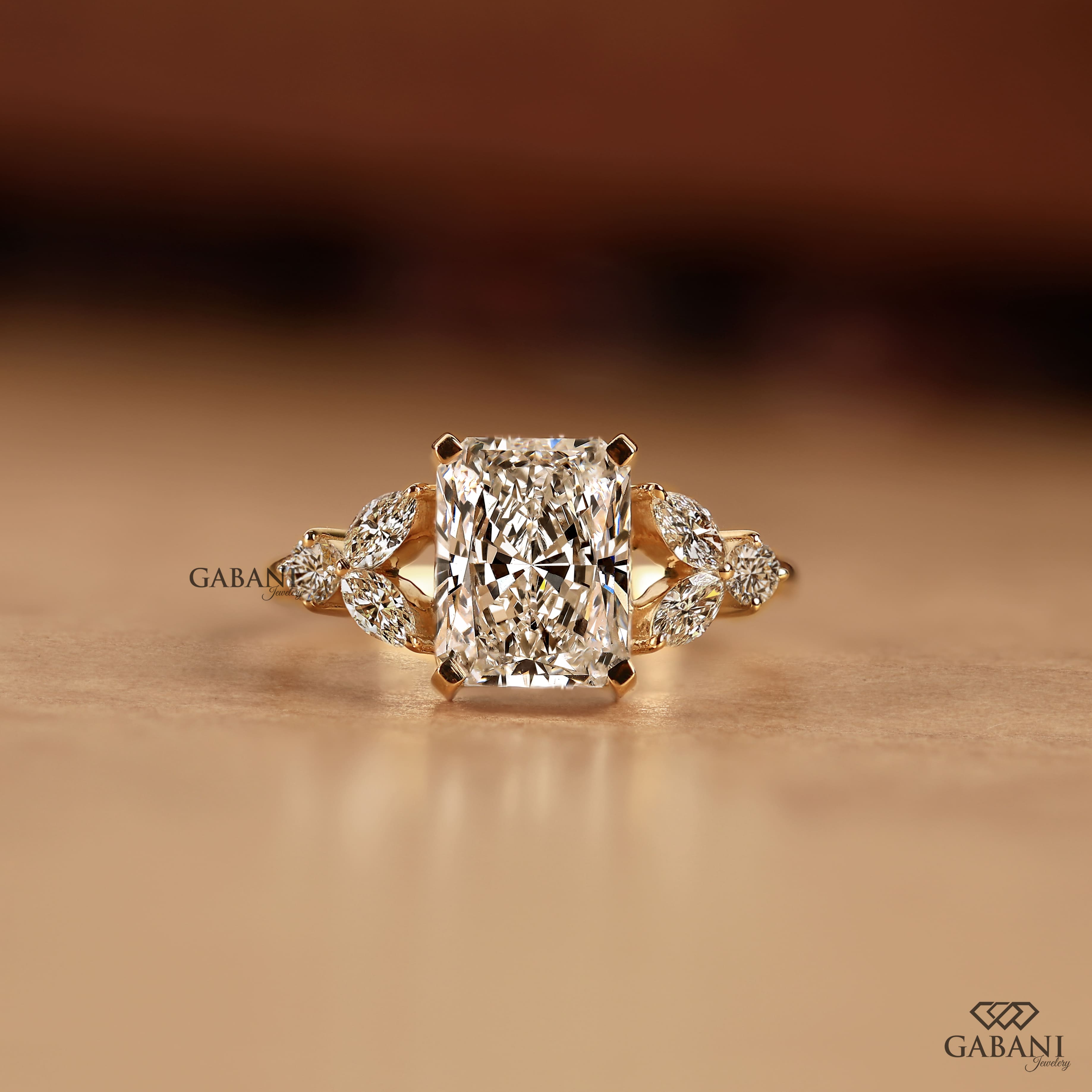 Radiant cut lab grown diamond engagement ring with marquise and round side diamond accents in a nature inspired gold setting.