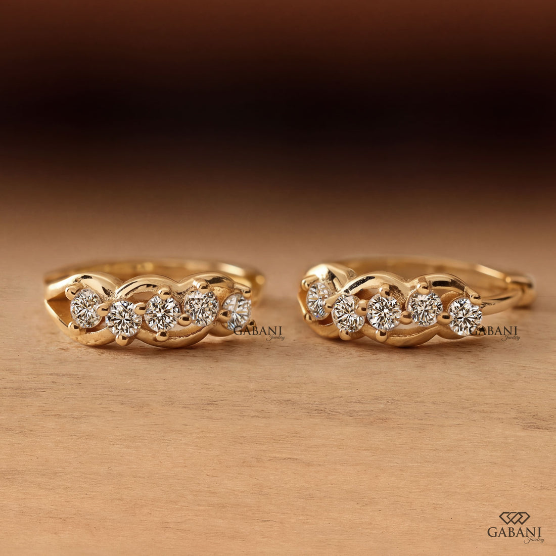 Round diamond infinity huggie hoop earrings in yellow gold with five diamonds and curved gold loop detailing.