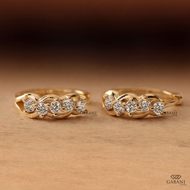 Round diamond infinity huggie hoop earrings in yellow gold with five diamonds and curved gold loop detailing.
