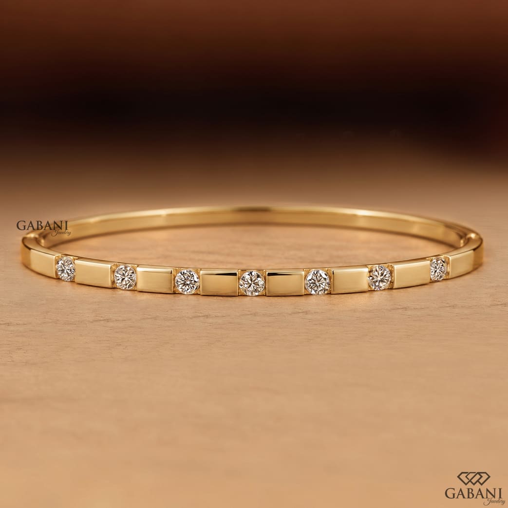 a round lab grown diamond bangle bracelet in yellow gold, featuring evenly spaced sparkling diamonds between polished gold bars in a modern geometric design by Gabani Jewelry.