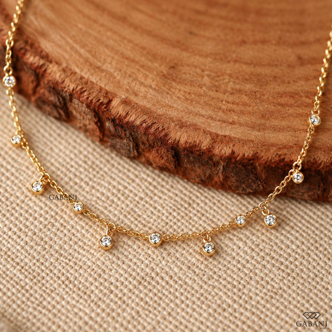 Round cut lab grown diamond station necklace with equal size bezel set diamonds and dangling diamond charms in 18K yellow gold.