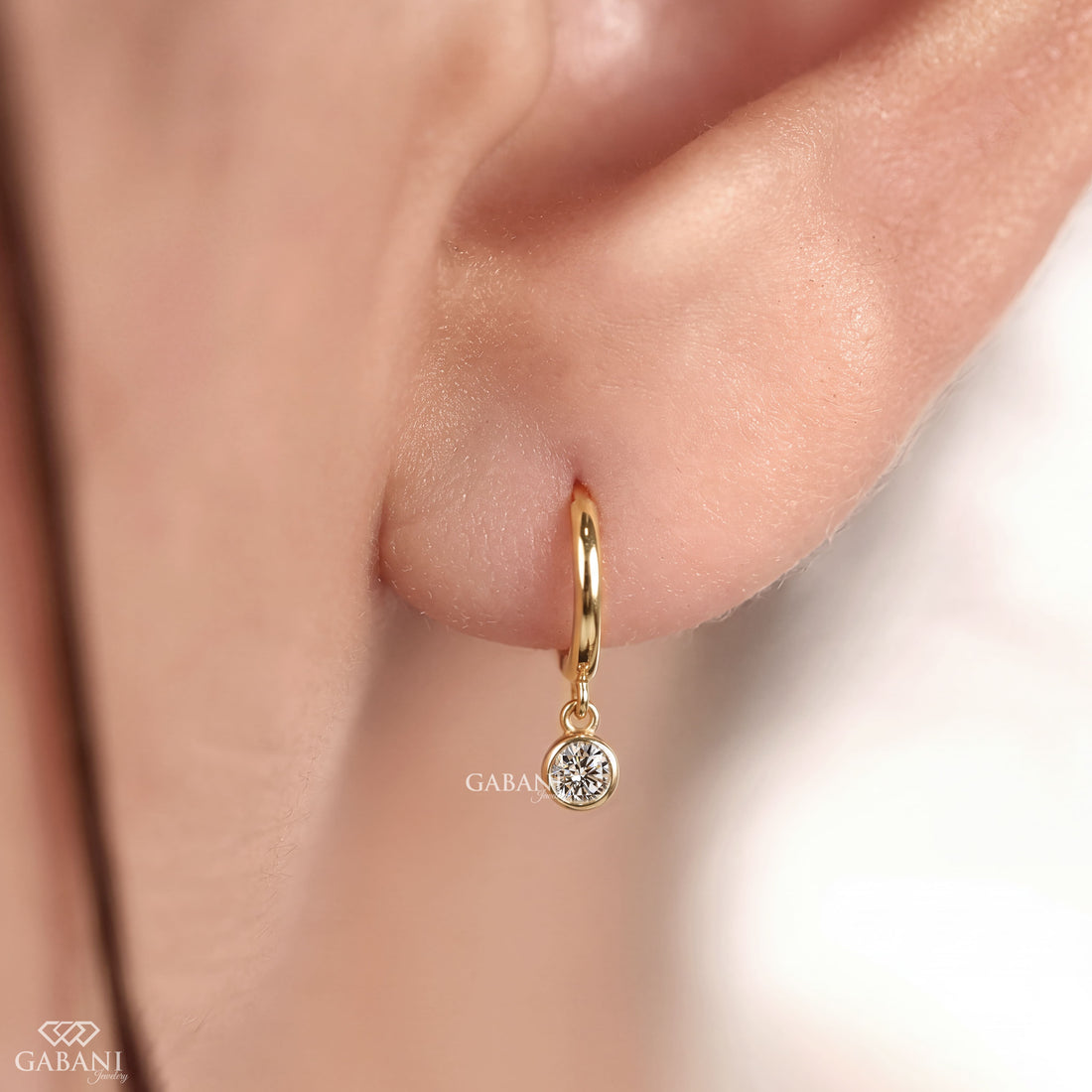 Round lab grown diamond bezel drop huggie earrings in yellow gold with 5 mm diamonds and hinged hoop closure.