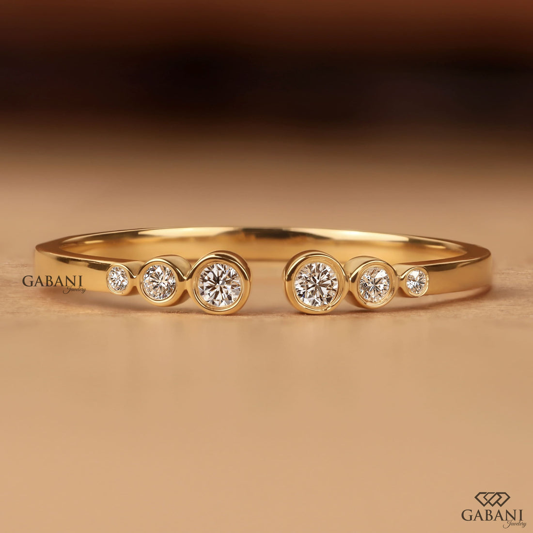 a round cut lab grown diamond open cuff band featuring six graduated bezel set diamonds in polished 14K yellow gold, a modern minimalist diamond wedding band by Gabani Jewelry.