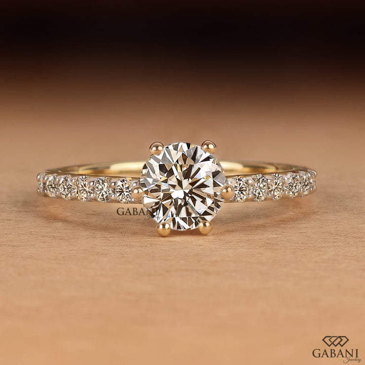 Round cut lab grown diamond solitaire engagement ring in yellow gold featuring a classic six prong setting and pavé diamond band.