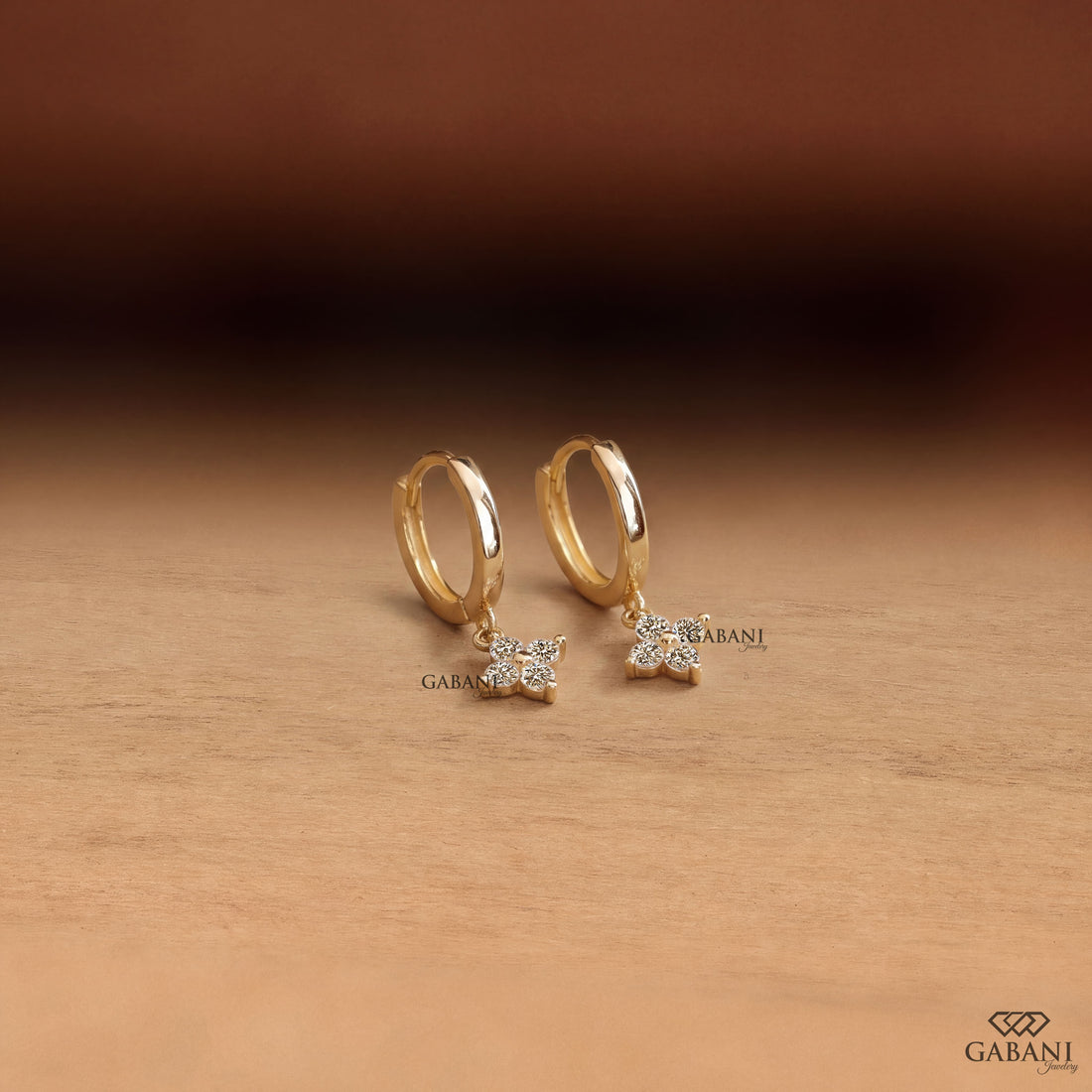 Close-up of round cut lab grown diamond flower charm huggie hoop earrings with four stone floral clusters in polished 18K yellow gold.