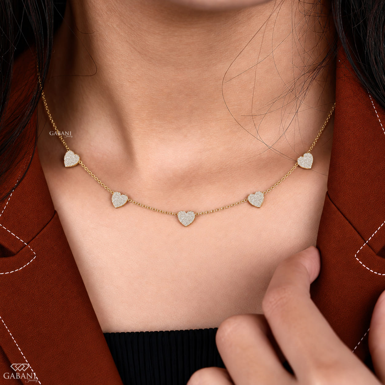 Dainty gold necklace with five sparkling heart charms covered in small round pavé set diamonds on a fine chain.