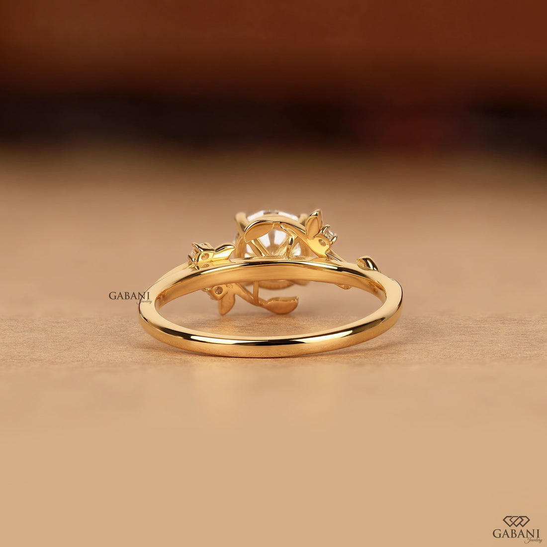 Round cut lab grown diamond engagement ring with floral leaf details, round side stones, four-prong setting, and yellow gold band.