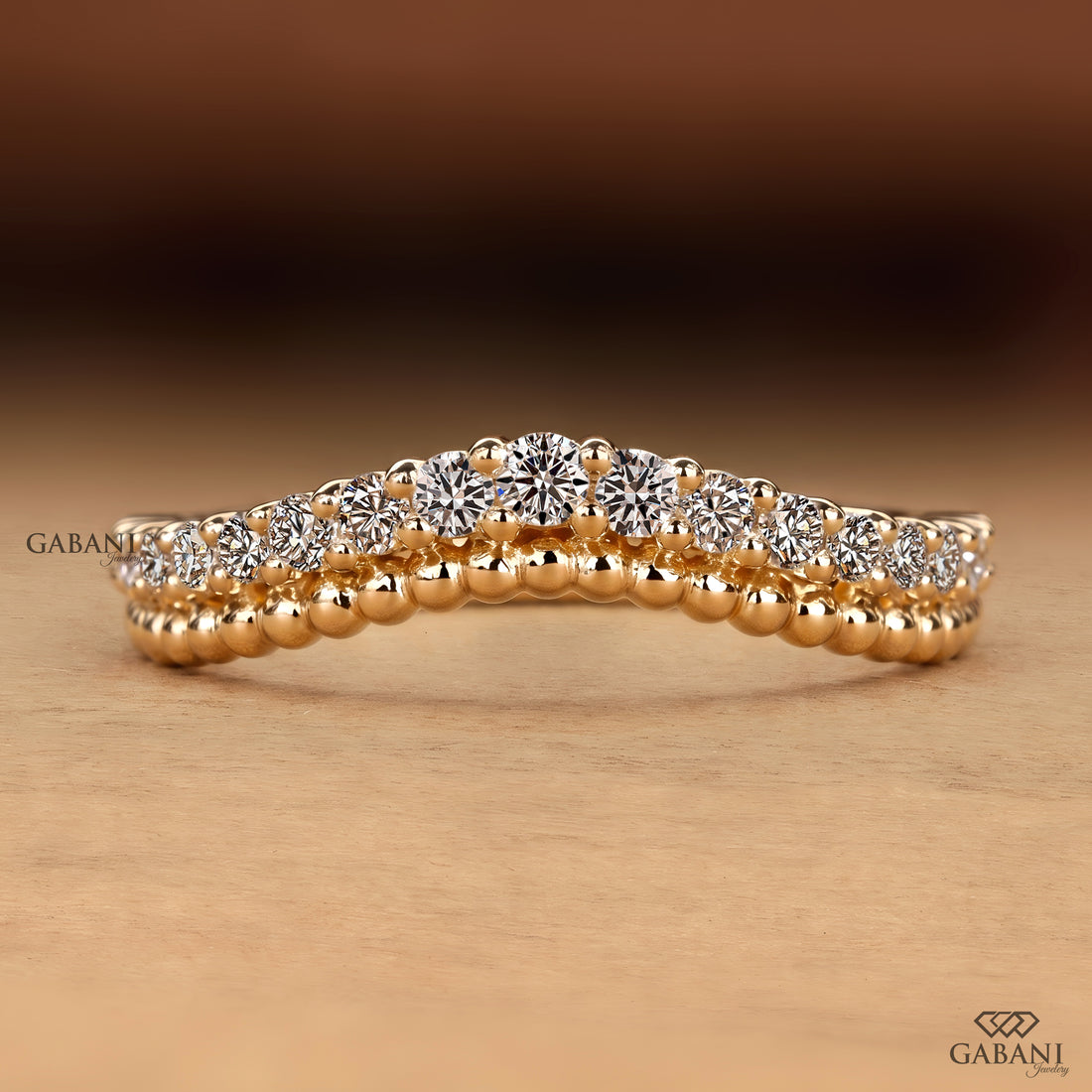 A close-up of a rose gold ring with a double row of round brilliant-cut diamonds, set against a warm brown and beige gradient background. The Gabani brand logo is visible in the bottom right corner.