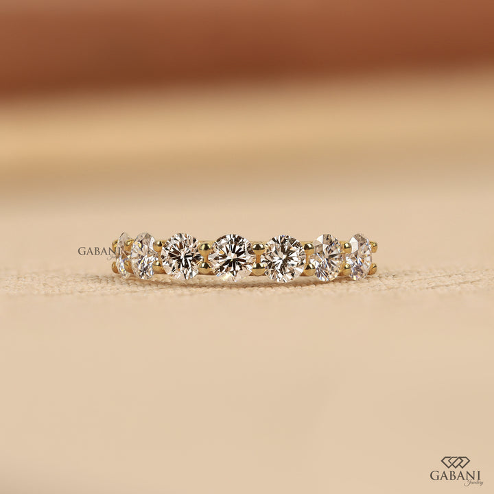 seven round cut lab grown diamonds in a yellow gold half eternity wedding band with open prong settings and a smooth shank.