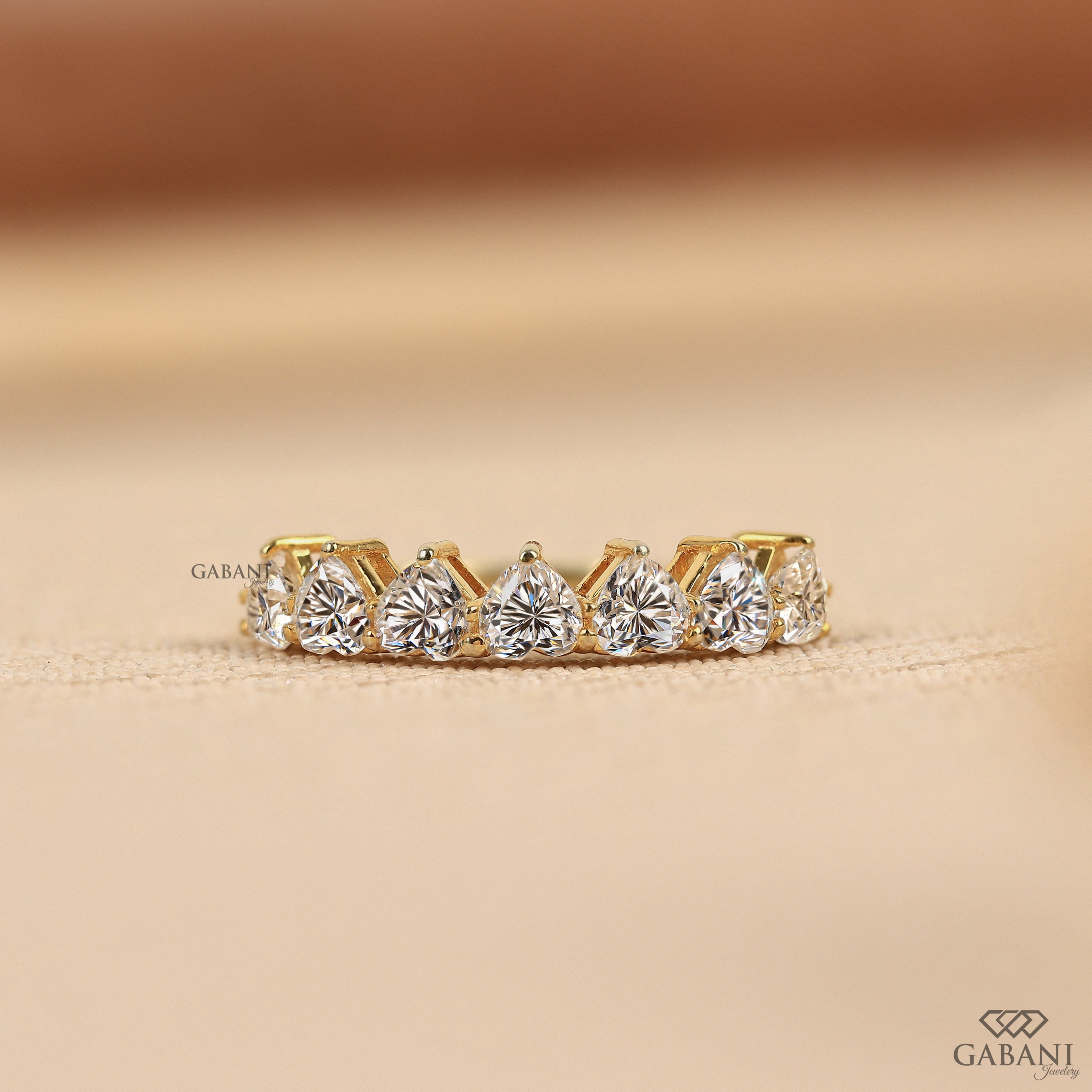 seven heart cut lab grown diamonds in a yellow gold half eternity wedding band with delicate prong settings.
