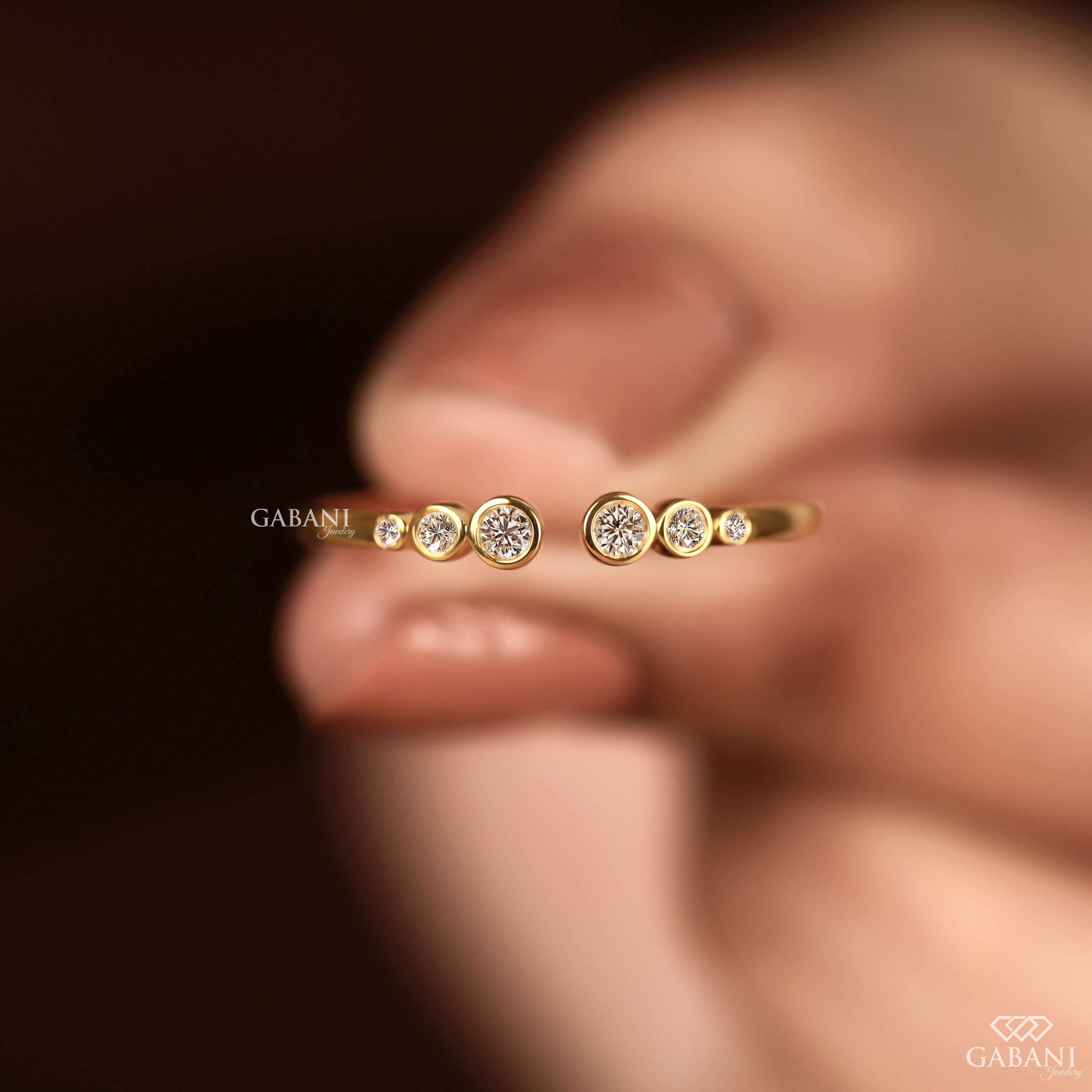 a round cut lab grown diamond open cuff band featuring six graduated bezel set diamonds in polished 14K yellow gold, a modern minimalist diamond wedding band by Gabani Jewelry.