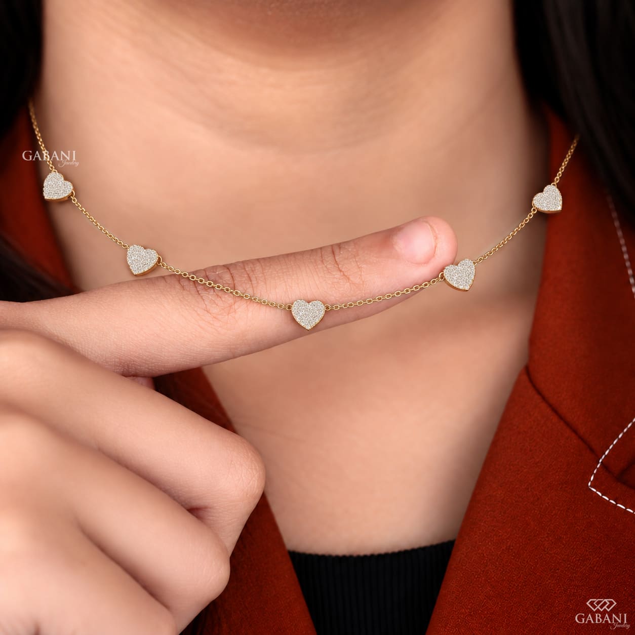 Dainty gold necklace with five sparkling heart charms covered in small round pavé set diamonds on a fine chain.