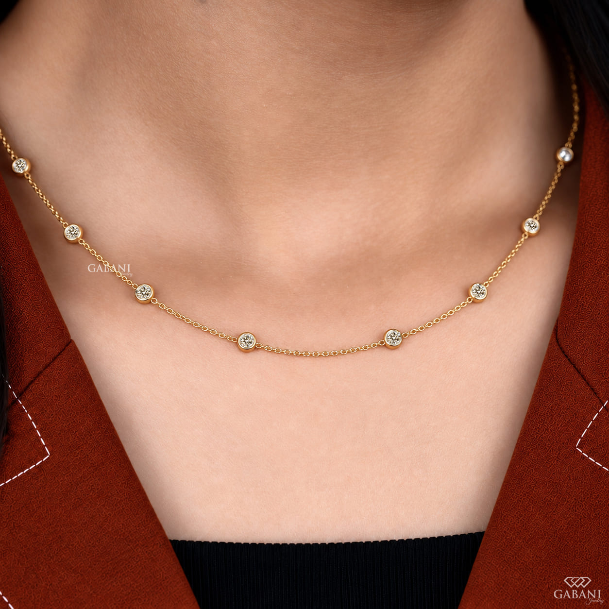 Yellow gold station necklace featuring evenly spaced round cut diamonds in full bezel settings along a delicate gold chain.