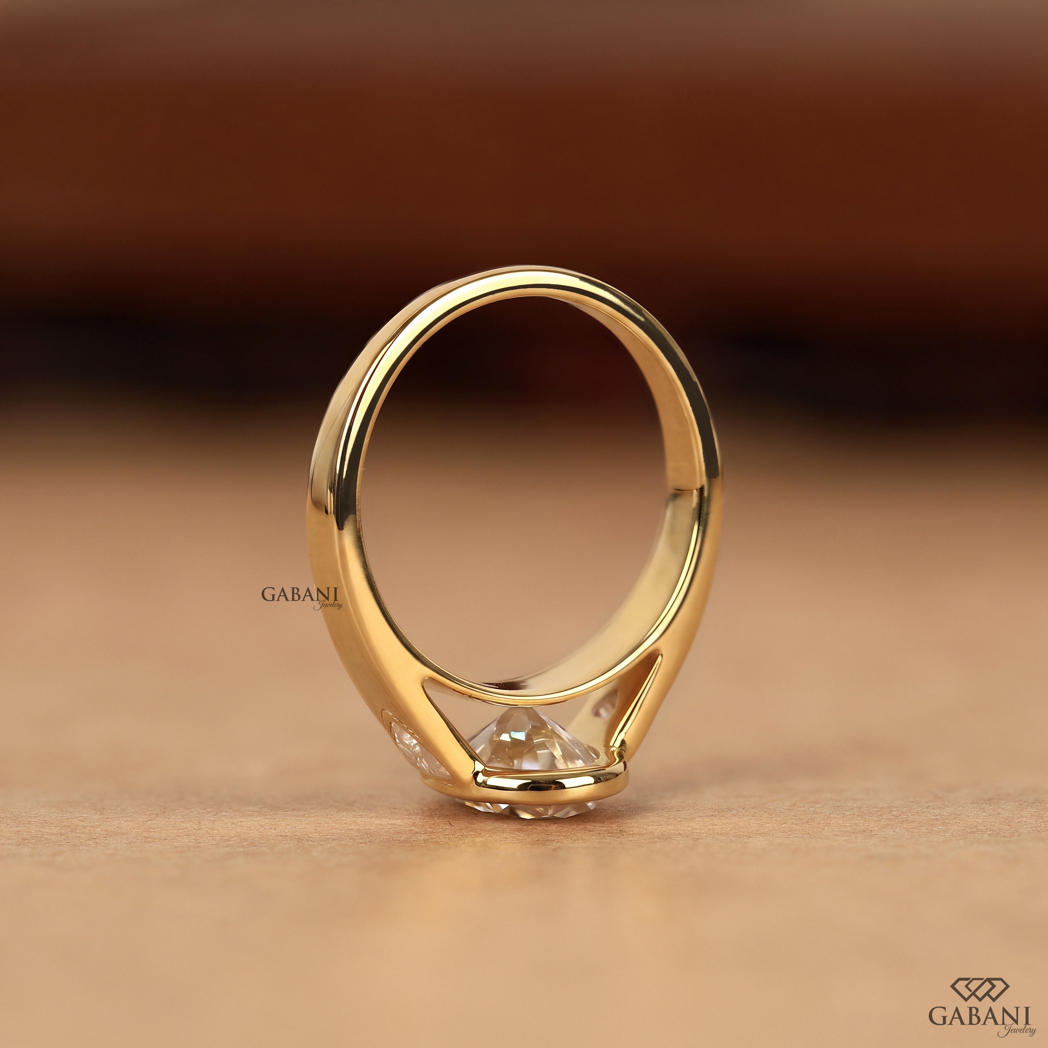 Standing view of an oval cut lab grown diamond three stone ring in solid yellow gold with a bezel set design