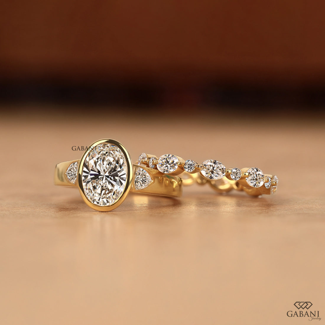 Display view of a three stone oval cut lab grown diamond engagement ring with bezel settings and trillion side diamonds