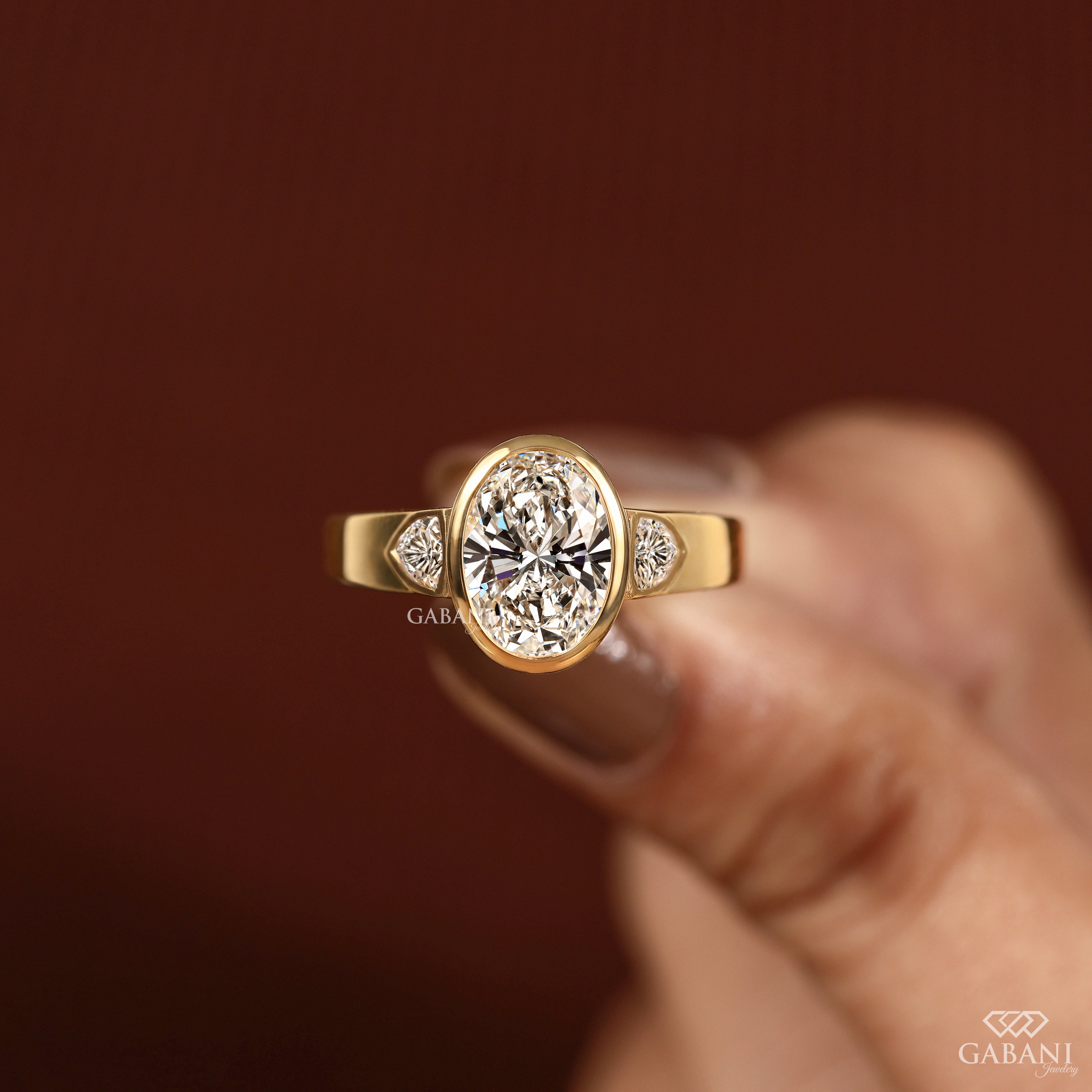 Display view of a three stone oval cut lab grown diamond engagement ring with bezel settings and trillion side diamonds