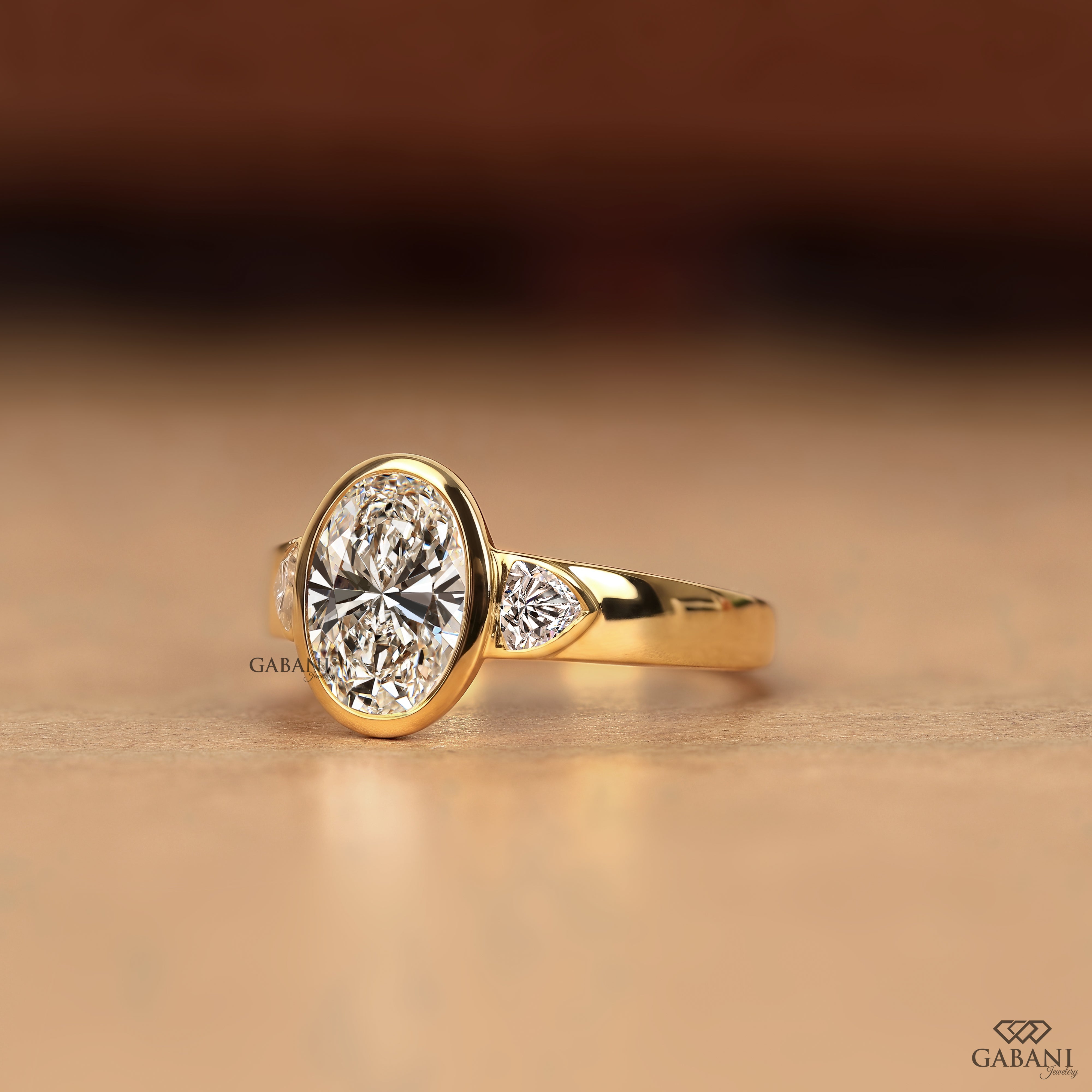 Side view of an oval bezel set lab grown diamond engagement ring with trillion side diamonds in solid yellow gold