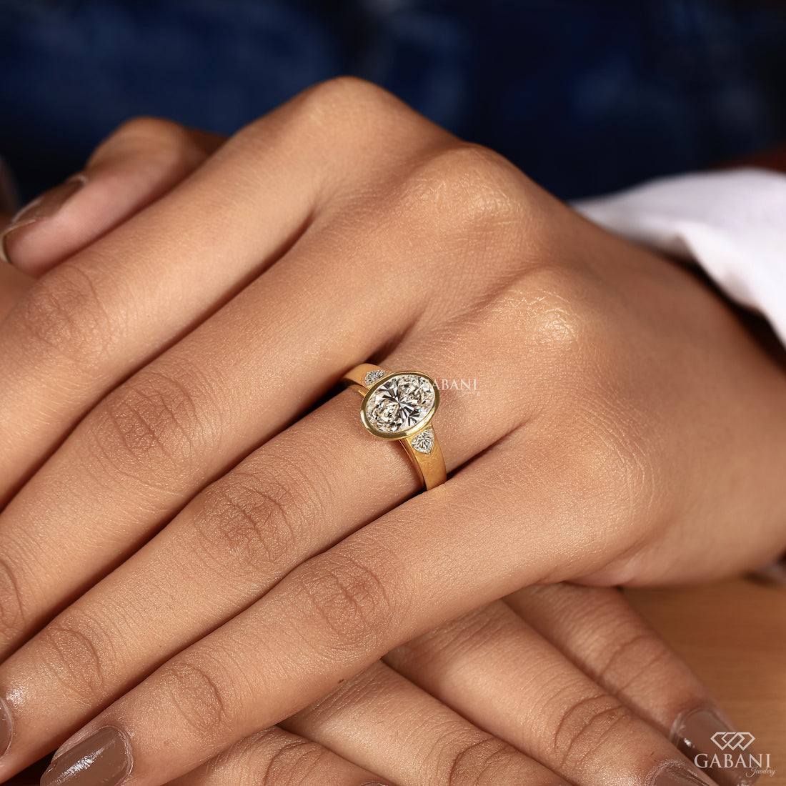 Hand model wearing an oval cut lab grown diamond engagement ring with trillion side diamonds in solid yellow gold